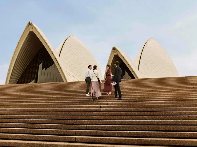 Vier mensen staan op de trappen voor het Sydney Opera House.