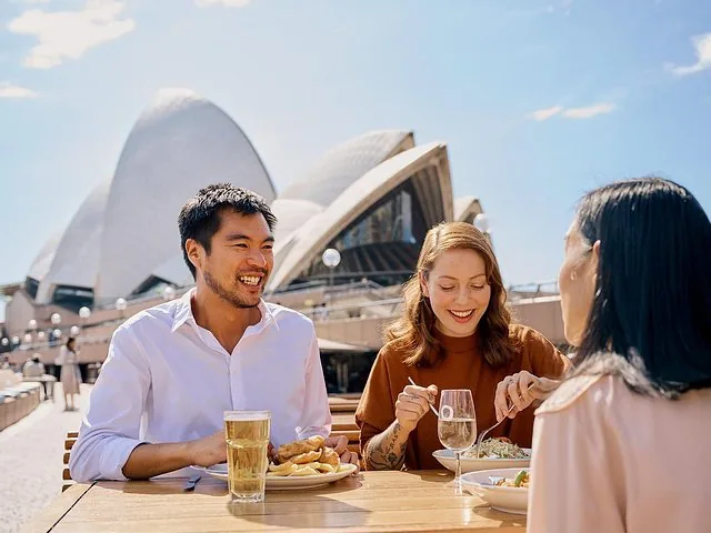 Vrienden genieten buiten van een maaltijd met het Sydney Opera House op de achtergrond.